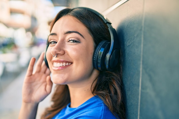 Jovem hispânica sorrindo feliz ouvindo música usando fones de ouvido na cidade