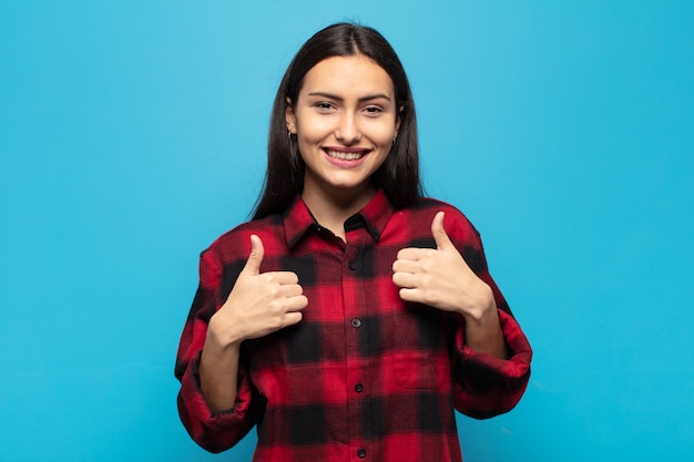 Jovem hispânica sorrindo, parecendo feliz, positiva, confiante e bem-sucedida, com os dois polegares para cima