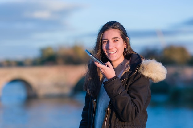 Jovem hispânica usa smartphone para redes sociais perto do rio tajo toledo estilo frio de inverno