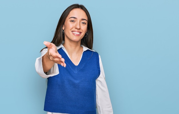 Jovem hispânica vestindo roupas casuais sorrindo amigável oferecendo aperto de mão como saudação e boas-vindas. negócio de sucesso.