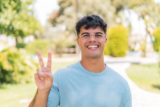 Foto jovem hispânico ao ar livre com óculos e fazendo sinal de ok