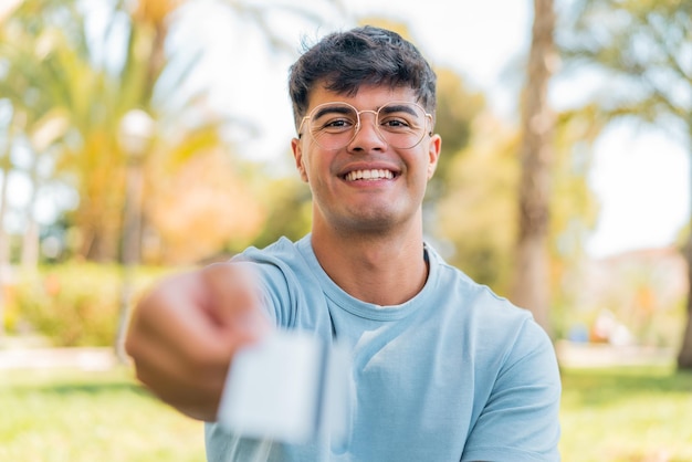 Jovem hispânico ao ar livre segurando um cartão de crédito com expressão feliz