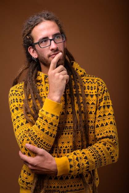 Jovem hispânico bonito com dreadlocks contra o fundo marrom