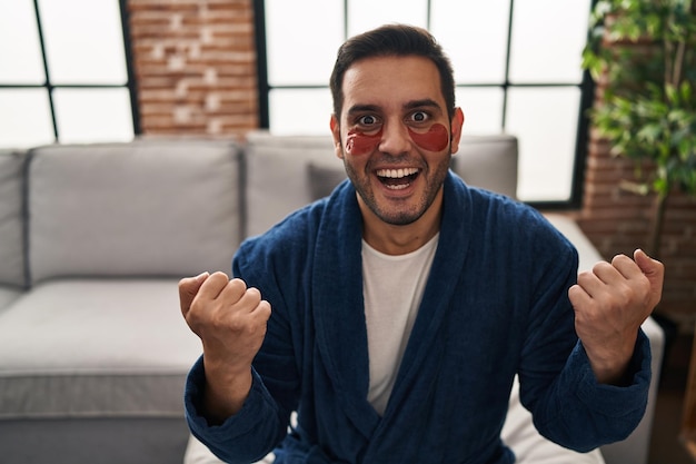 Jovem hispânico com barba usando tapa-olhos de beleza gritando orgulhoso, comemorando a vitória e o sucesso muito animado com os braços erguidos