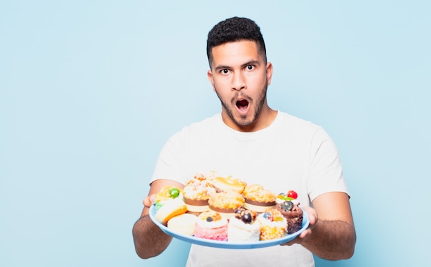 Jovem hispânico com expressão de medo segurando cupcakes