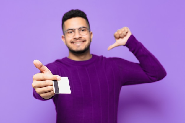 Jovem hispânico com expressão feliz e segurando um cartão de crédito