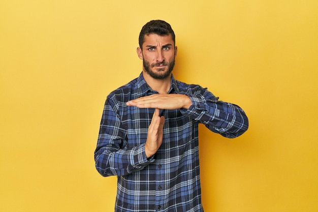 Jovem hispânico em fundo amarelo mostrando um gesto de tempo limite