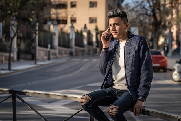 Jovem hispânico falando com smartphone, vestido com jeans e jaqueta casual