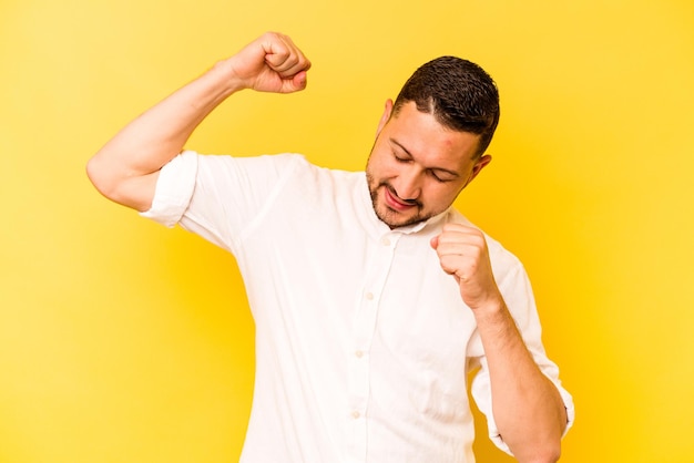 Jovem hispânico isolado em fundo amarelo comemorando um dia especial salta e levanta os braços com energia