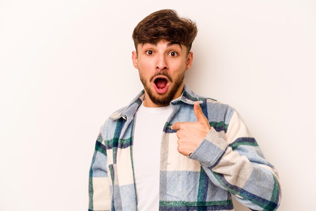 Jovem hispânico isolado no fundo branco surpreendeu apontando com o dedo sorrindo amplamente