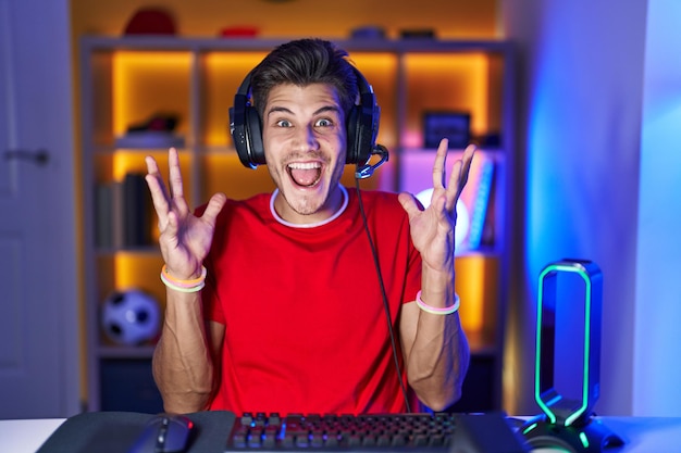 Foto jovem hispânico jogando videogame comemorando louco e surpreso pelo sucesso com os braços levantados e olhos abertos gritando o conceito de vencedor animado