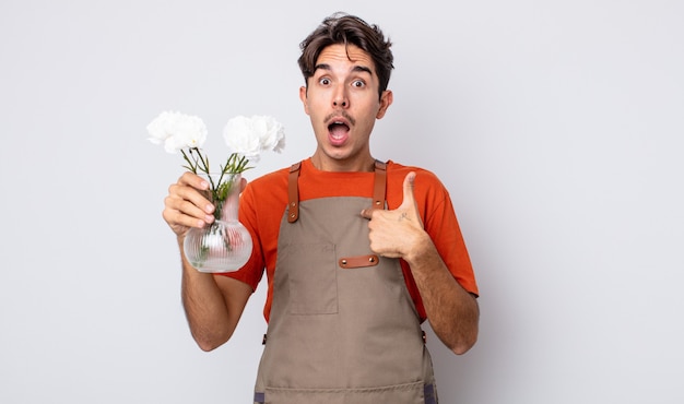 Jovem hispânico parecendo chocado e surpreso com a boca aberta, apontando para si mesmo. conceito de florista