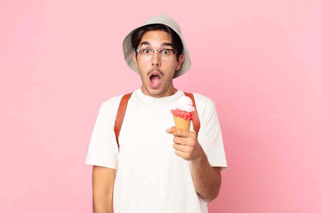 Jovem hispânico parecendo muito chocado ou surpreso e segurando um sorvete