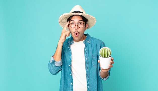 Jovem hispânico parecendo surpreso, percebendo um novo pensamento, ideia ou conceito e segurando um cacto