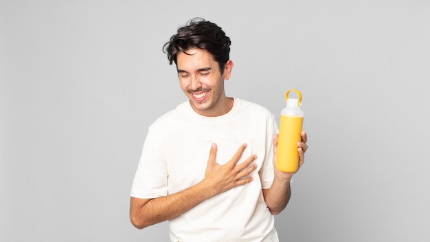 Jovem hispânico rindo alto de uma piada hilária com uma garrafa térmica de café
