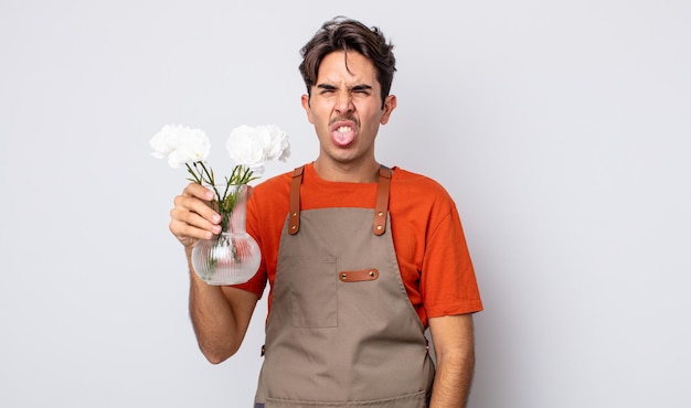 Jovem hispânico se sentindo enojado e irritado e com a língua de fora. conceito de florista