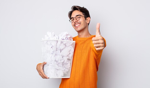 Jovem hispânico se sentindo orgulhoso, sorrindo positivamente com os polegares para cima. conceito de lixo de bolas de papel