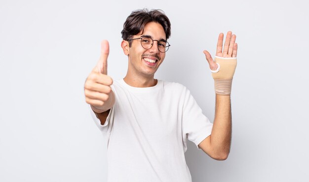 Jovem hispânico, sentindo-se orgulhoso, sorrindo positivamente com o polegar para cima. conceito de bandagem de mão