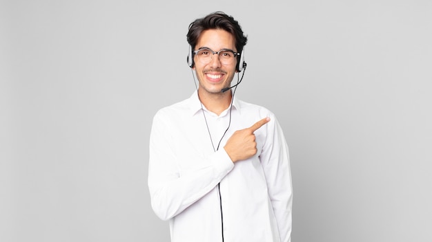 Jovem hispânico sorrindo alegremente, sentindo-se feliz e apontando para o lado. conceito de telemarketing