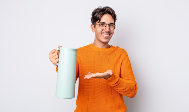 Jovem hispânico sorrindo alegremente, sentindo-se feliz e mostrando um conceito. conceito de garrafa térmica