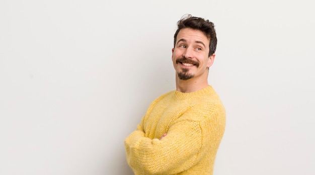 Jovem hispânico sorrindo alegremente sentindo-se feliz satisfeito e relaxado com os braços cruzados e olhando para o lado