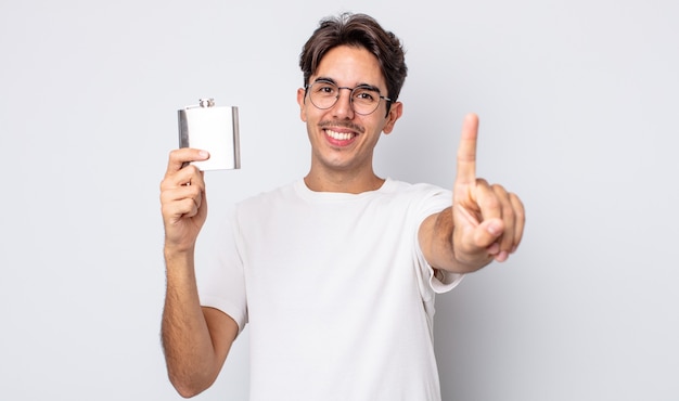 Foto jovem hispânico sorrindo com orgulho e confiança fazendo o número um. conceito de frasco de álcool