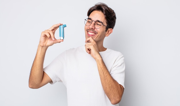 Jovem hispânico sorrindo com uma expressão feliz e confiante com a mão no queixo. conceito de asma