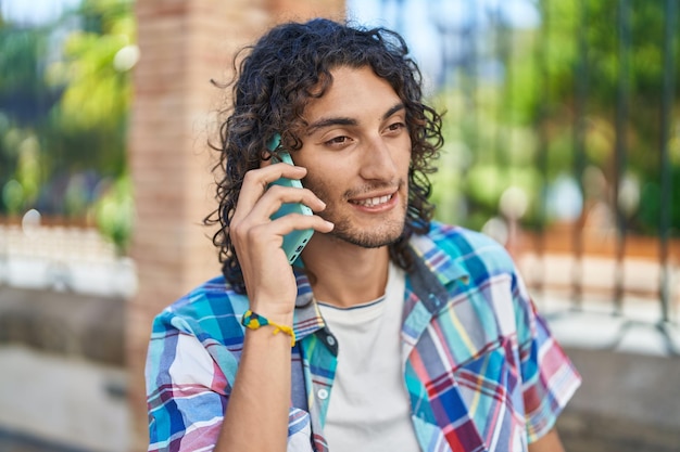 Jovem hispânico sorrindo confiante falando no smartphone na rua