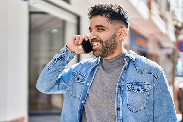 Jovem hispânico sorrindo confiante falando no smartphone na rua