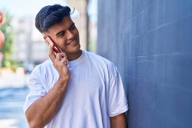 Jovem hispânico sorrindo confiante falando no smartphone na rua