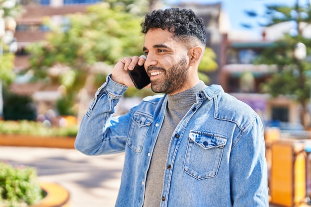 Jovem hispânico sorrindo confiante falando no smartphone no parque