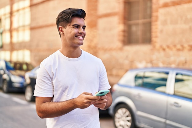 Jovem hispânico sorrindo confiante usando smartphone na rua