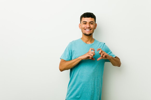 Jovem hispânico, sorrindo e mostrando uma forma de coração com as mãos