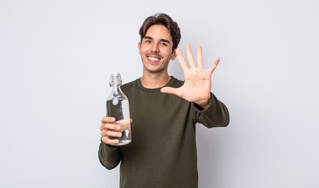 Jovem hispânico sorrindo e parecendo amigável, mostrando o número cinco. conceito de garrafa de água