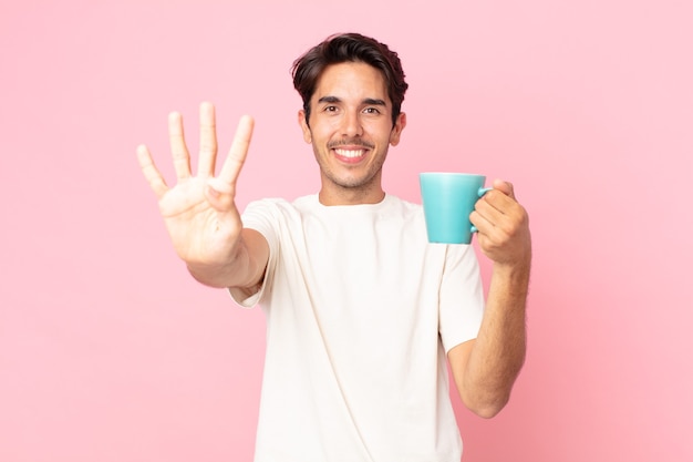 Jovem hispânico sorrindo e parecendo amigável, mostrando o número quatro e segurando uma caneca de café