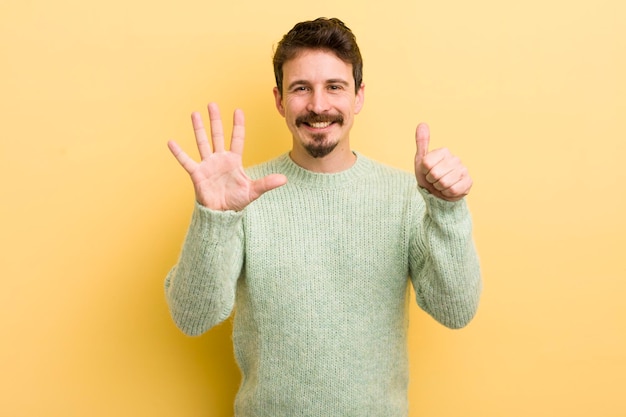 Jovem hispânico sorrindo e parecendo amigável, mostrando o número seis ou sexto com a mão em contagem regressiva