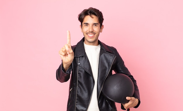 Jovem hispânico sorrindo e parecendo amigável, mostrando o número um. conceito de motociclista