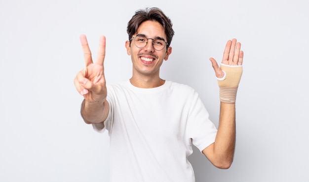 jovem hispânico sorrindo e parecendo feliz, gesticulando vitória ou paz. conceito de bandagem de mão