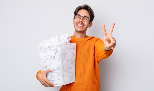 Jovem hispânico sorrindo e parecendo feliz, gesticulando vitória ou paz. conceito de lixo de bolas de papel