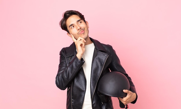 Jovem hispânico sorrindo feliz e sonhando acordado ou duvidando. conceito de motociclista