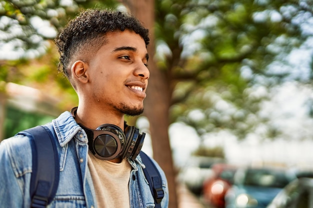 Jovem hispânico sorrindo usando fones de ouvido no campus da universidade