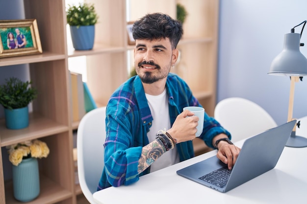 Jovem hispânico usando laptop e tomando café em casa