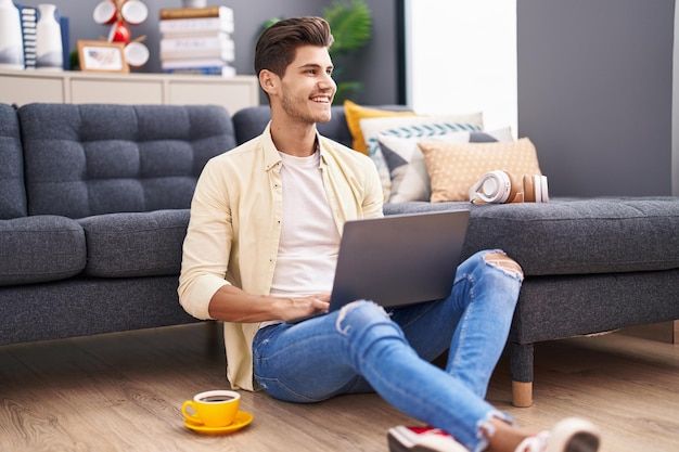 Jovem hispânico usando laptop sentado no chão em casa