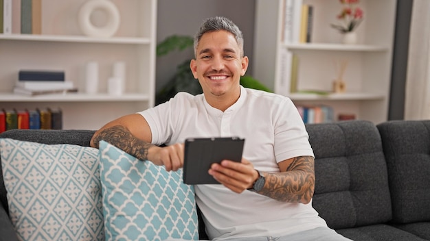 Jovem hispânico usando touchpad sentado no sofá em casa