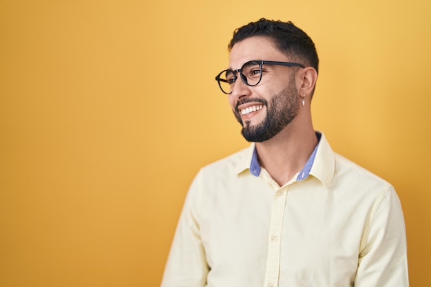 Jovem hispânico vestindo roupas de negócios e óculos olhando para o lado com sorriso no rosto expressão natural rindo confiante