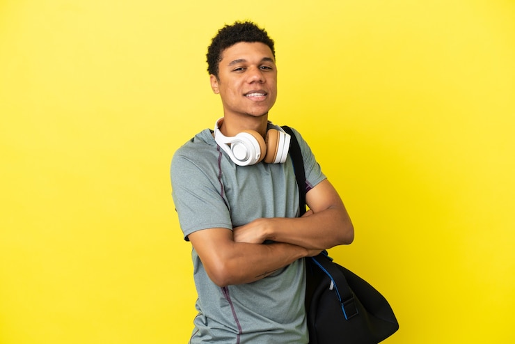 Foto jovem homem afro-americano com uma bolsa esportiva isolada em um fundo amarelo com os braços cruzados e olhando para a frente