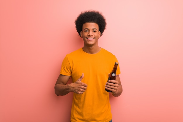 Jovem, homem americano africano, segurando, um, cerveja, divertimento, e, feliz, fazendo, um, gesto, de, vitória