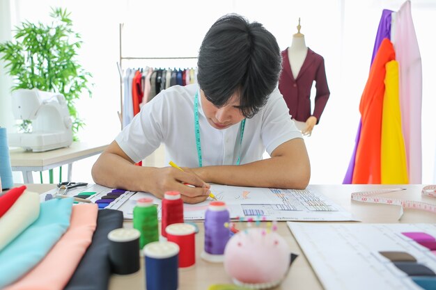 Jovem homem asiático segurando o lápis e desenhando o esboço do modelo na mesa no ateliê.