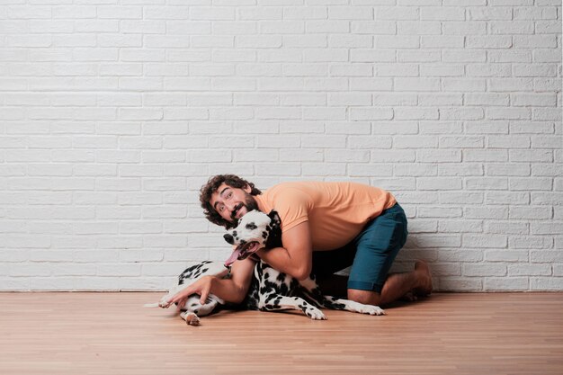 Jovem homem barbudo com um cachorro dálmata contra a parede de tijolos brancos