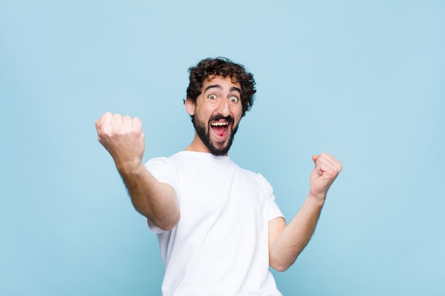 Jovem homem barbudo louco gritando triunfantemente, parecendo vencedor animado, feliz e surpreso, comemorando